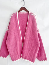 Load image into Gallery viewer, Pink knitted cardigan with white trim on a wooden hanger against a white background